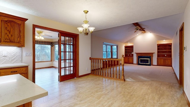 unfurnished dining area featuring ceiling fan with notable chandelier, a textured ceiling, vaulted ceiling with beams, and light carpet