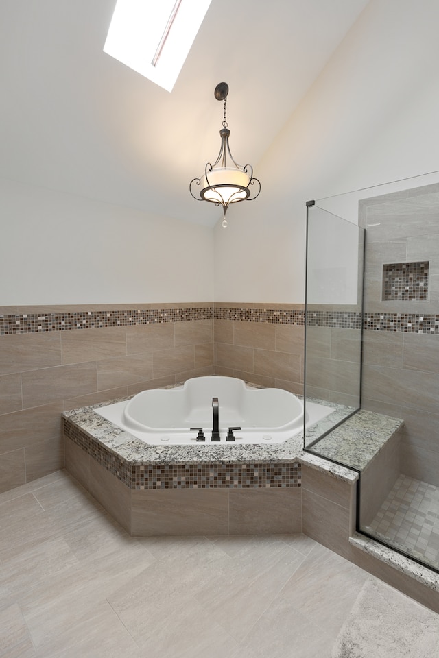 bathroom featuring separate shower and tub, vaulted ceiling with skylight, tile walls, and tile patterned floors