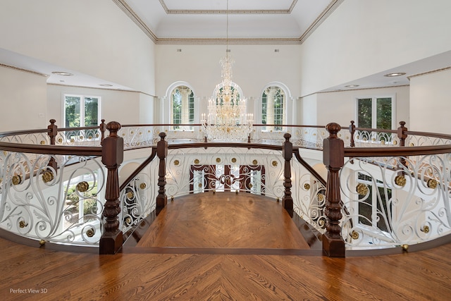 staircase featuring crown molding, a high ceiling, a tray ceiling, wood-type flooring, and a chandelier