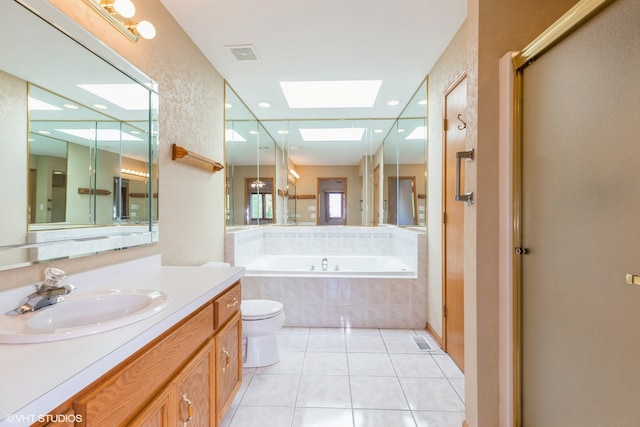 bathroom featuring a skylight, toilet, tile patterned floors, a relaxing tiled tub, and vanity