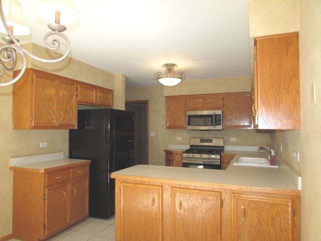 kitchen with stainless steel appliances, kitchen peninsula, light tile patterned flooring, and sink