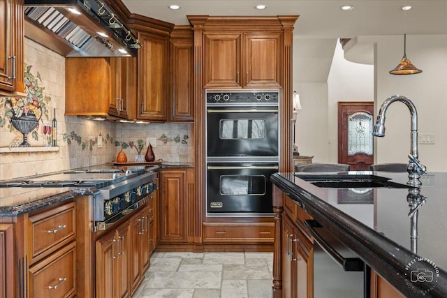 kitchen featuring double oven, dark stone countertops, wall chimney range hood, and stainless steel gas cooktop