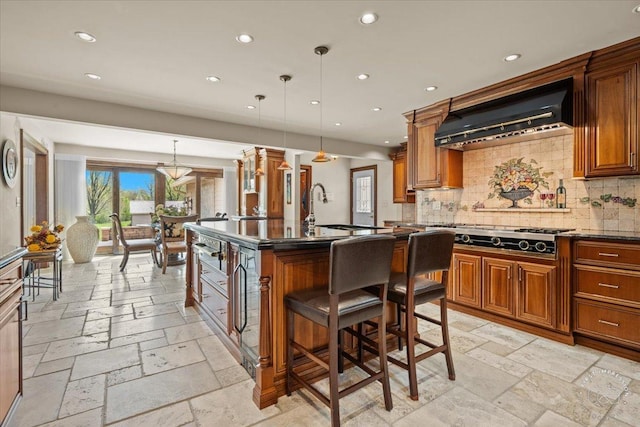 kitchen featuring hanging light fixtures, a kitchen breakfast bar, an island with sink, dark stone counters, and exhaust hood