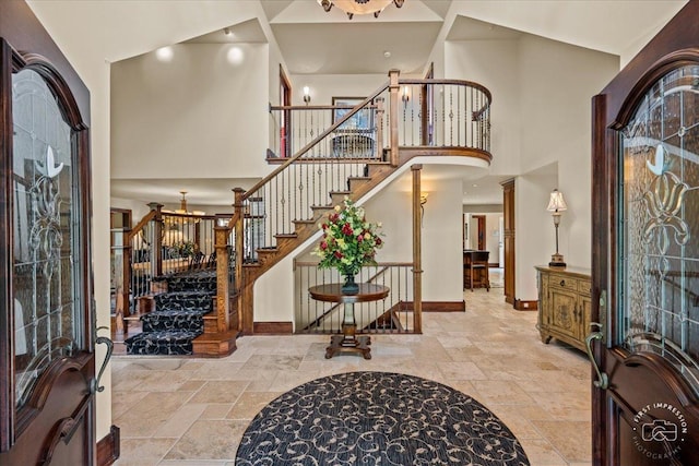 entrance foyer with stone tile flooring, a towering ceiling, baseboards, stairs, and decorative columns