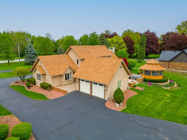 view of front facade featuring driveway, a garage, stone siding, a gazebo, and a front yard