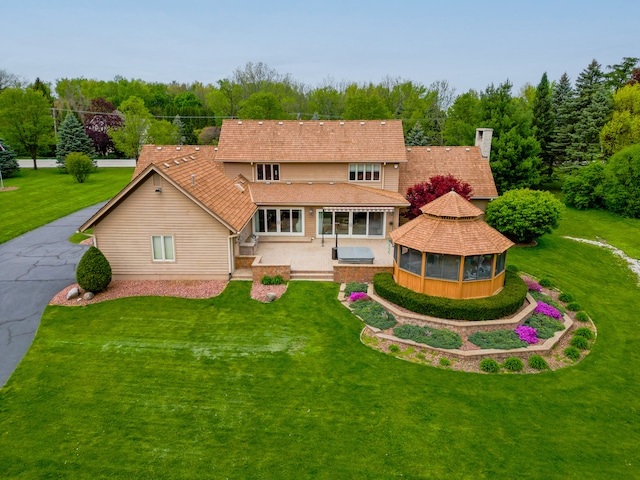 rear view of house featuring driveway, a chimney, a lawn, and a gazebo