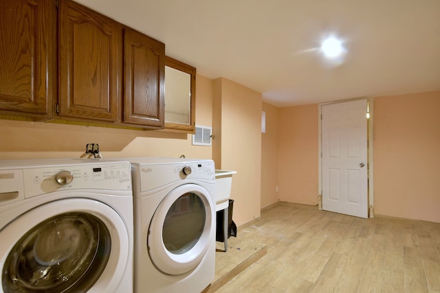 laundry area featuring light hardwood / wood-style floors, washer and dryer, and cabinets