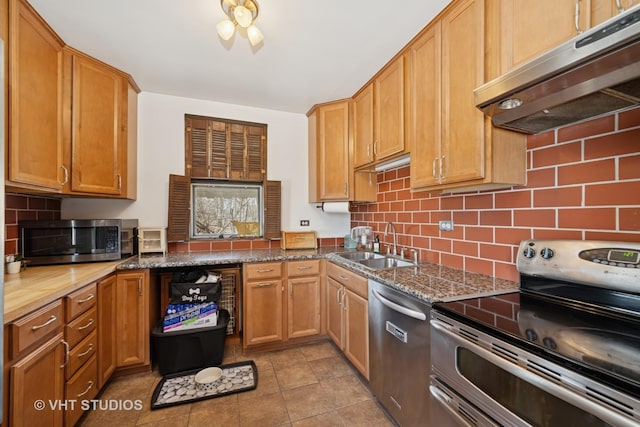 kitchen with light tile patterned flooring, a sink, decorative backsplash, extractor fan, and appliances with stainless steel finishes