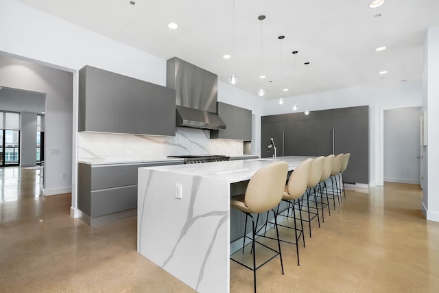 kitchen featuring pendant lighting, gray cabinetry, a large island, wall chimney exhaust hood, and a breakfast bar area