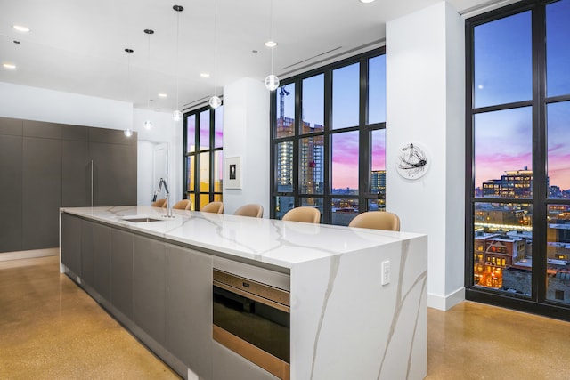 kitchen featuring a large island with sink, sink, pendant lighting, and light stone counters