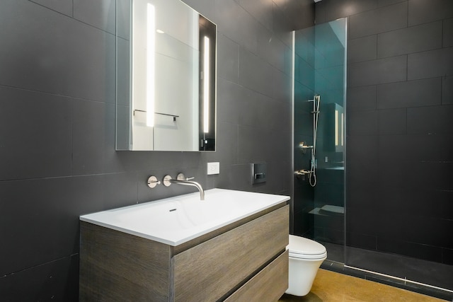 bathroom with tile walls, tiled shower, vanity, and toilet