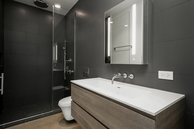 bathroom with a tile shower, vanity, tile walls, and toilet