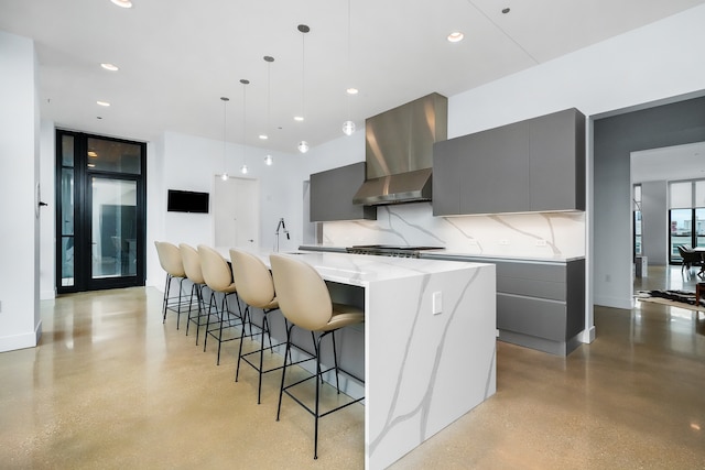 kitchen with gray cabinetry, tasteful backsplash, wall chimney exhaust hood, decorative light fixtures, and a large island