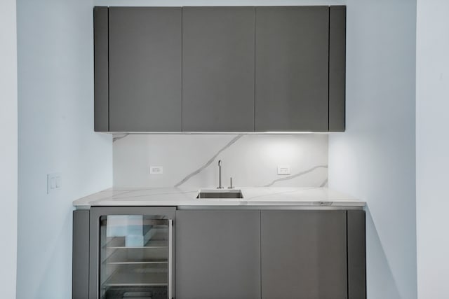 bar featuring gray cabinets, wine cooler, light stone counters, and sink