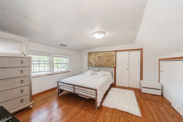 bedroom featuring light hardwood / wood-style floors, lofted ceiling, and a closet