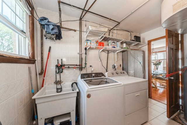 laundry area with tile walls, light tile patterned floors, separate washer and dryer, and sink