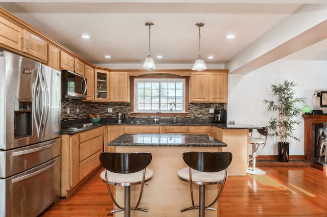 kitchen with appliances with stainless steel finishes, hanging light fixtures, a kitchen bar, a center island, and hardwood / wood-style floors