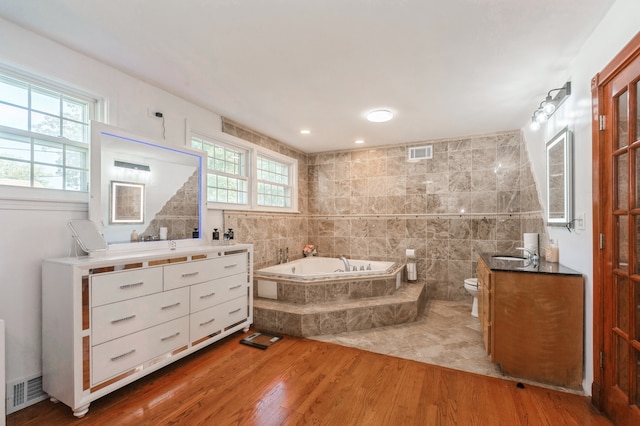 bathroom with tiled bath, vanity, hardwood / wood-style flooring, toilet, and plenty of natural light