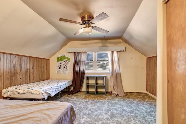 carpeted bedroom with wooden walls, vaulted ceiling, and ceiling fan