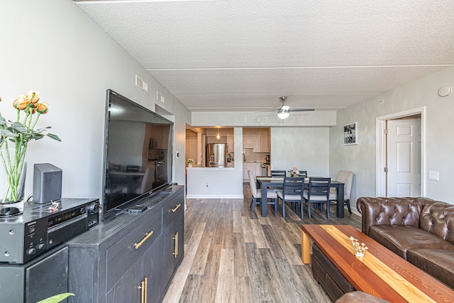 living room featuring ceiling fan, dark wood-type flooring, and a textured ceiling