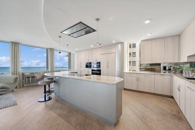 kitchen featuring hanging light fixtures, a water view, backsplash, a kitchen island, and stainless steel double oven