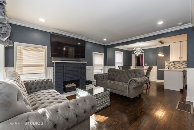 living room with dark hardwood / wood-style floors, ornamental molding, a fireplace, and an inviting chandelier