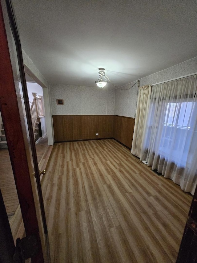 empty room with wooden walls, a textured ceiling, and hardwood / wood-style flooring