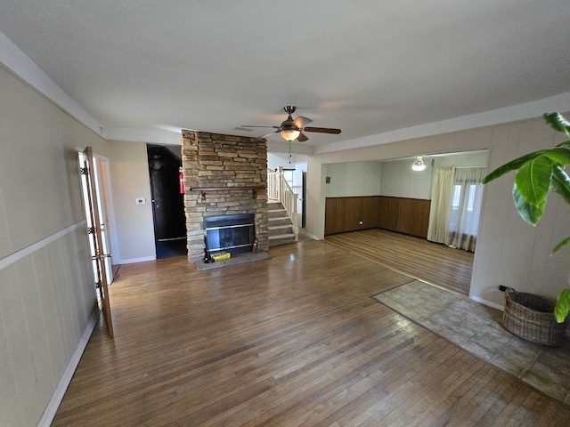 unfurnished living room featuring wood-type flooring, a stone fireplace, ceiling fan, and wood walls