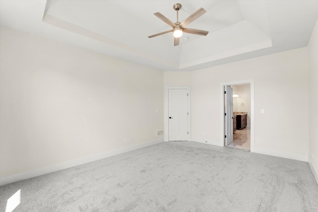 empty room featuring light colored carpet, ceiling fan, and a raised ceiling