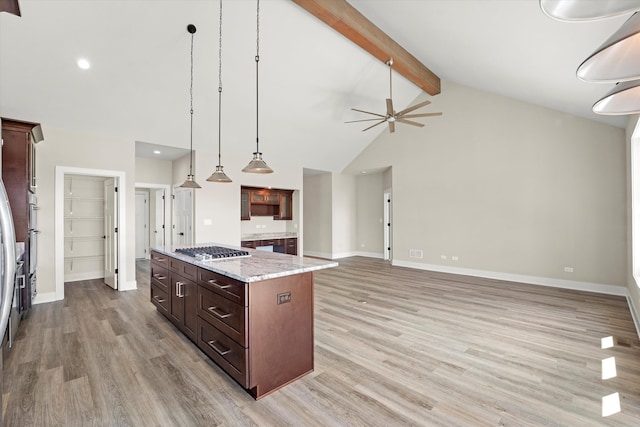 kitchen featuring ceiling fan, high vaulted ceiling, stainless steel gas stovetop, a center island, and light wood-type flooring