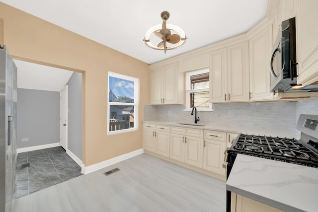 kitchen with cream cabinetry, decorative backsplash, sink, and range with gas cooktop