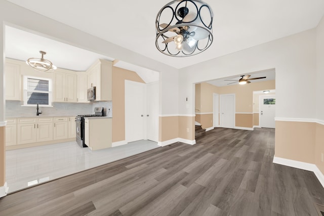 unfurnished living room featuring sink, ceiling fan with notable chandelier, and hardwood / wood-style floors