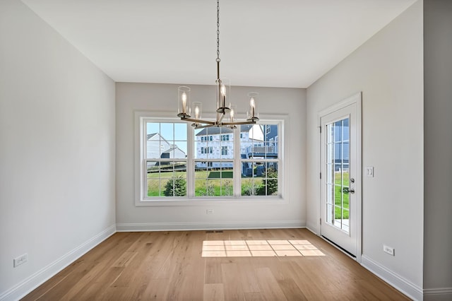 unfurnished dining area with baseboards, an inviting chandelier, and wood finished floors