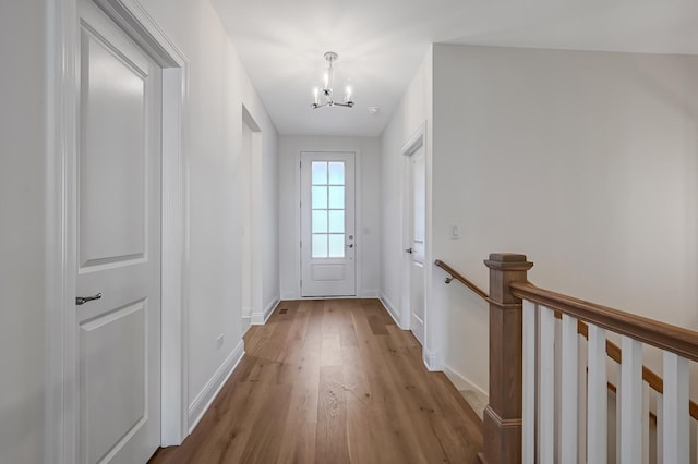 doorway to outside featuring baseboards, a chandelier, and wood finished floors