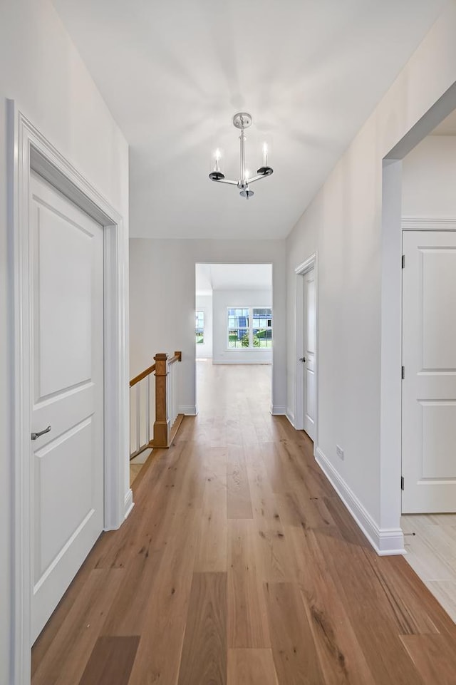 hallway with light wood-style flooring, an inviting chandelier, baseboards, and an upstairs landing