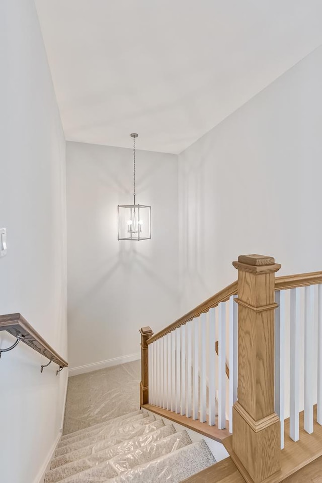 stairway with an inviting chandelier, baseboards, and carpet floors