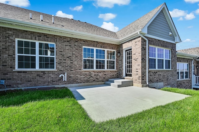 rear view of house with roof with shingles, a patio area, brick siding, and a lawn