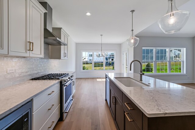 kitchen with wall chimney exhaust hood, a sink, appliances with stainless steel finishes, light wood-style floors, and backsplash
