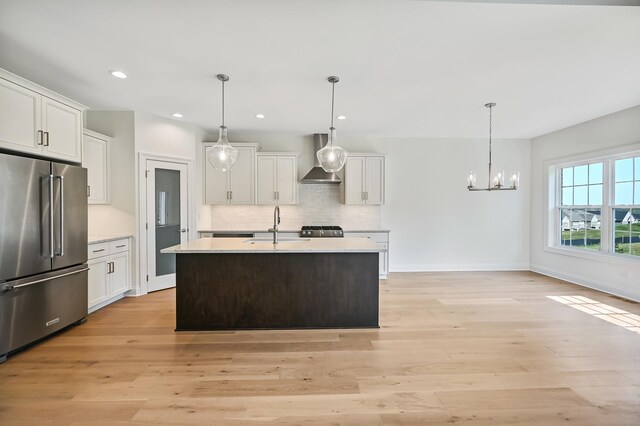 kitchen with wall chimney range hood, light countertops, a chandelier, high end refrigerator, and backsplash