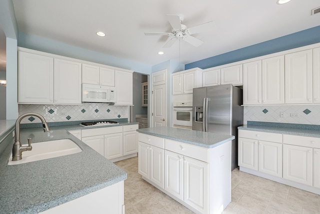 kitchen featuring sink, white cabinets, a kitchen island, decorative backsplash, and white appliances