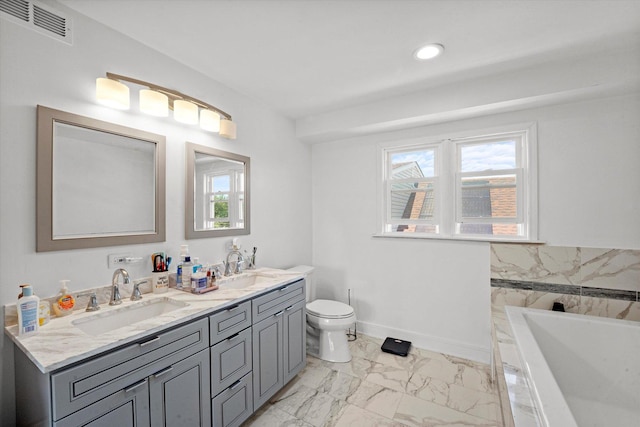 bathroom featuring marble look tiles, toilet, a tub, double vanity, and baseboards