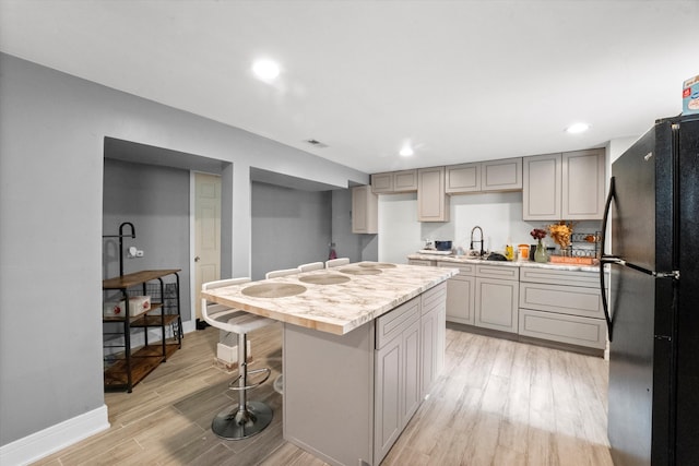 kitchen with gray cabinetry, light wood-type flooring, black refrigerator, and a center island