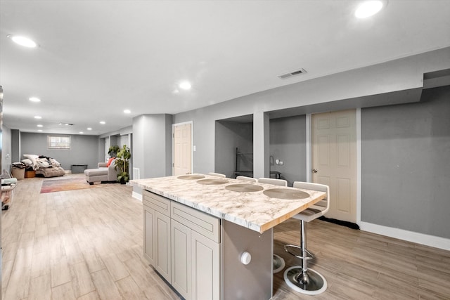 kitchen with light stone counters, light hardwood / wood-style floors, a kitchen bar, and a kitchen island