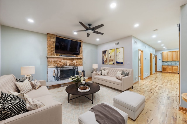 living room featuring light wood-type flooring, ceiling fan, and a stone fireplace