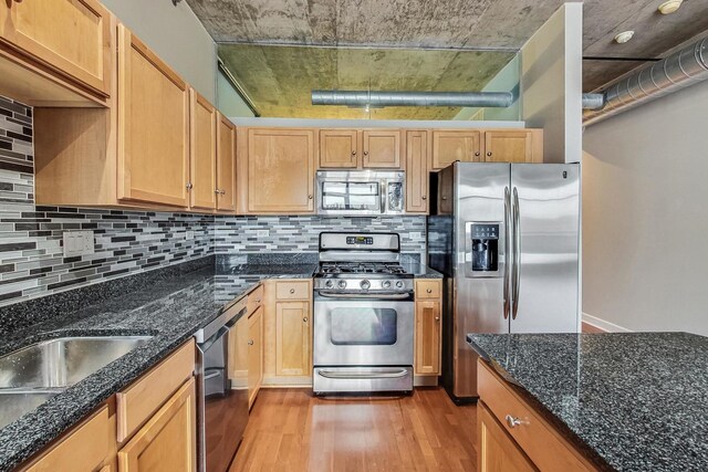 kitchen with dark stone counters, appliances with stainless steel finishes, tasteful backsplash, and light hardwood / wood-style flooring