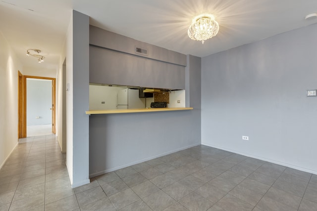 kitchen featuring a notable chandelier, kitchen peninsula, light tile patterned floors, and white refrigerator