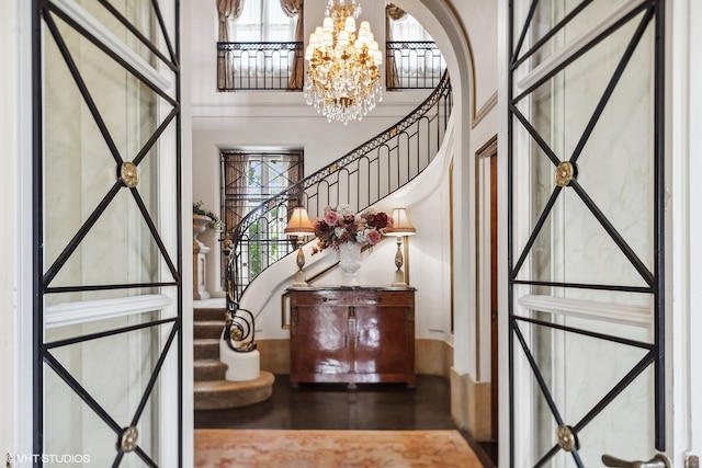 entryway with an inviting chandelier, a wealth of natural light, a towering ceiling, and dark hardwood / wood-style floors