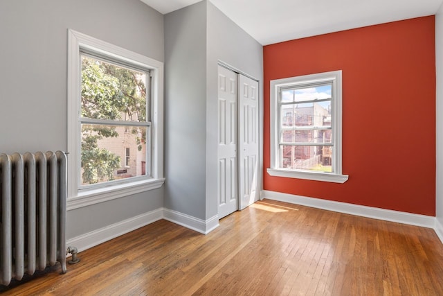 interior space with radiator heating unit, a closet, multiple windows, and hardwood / wood-style flooring