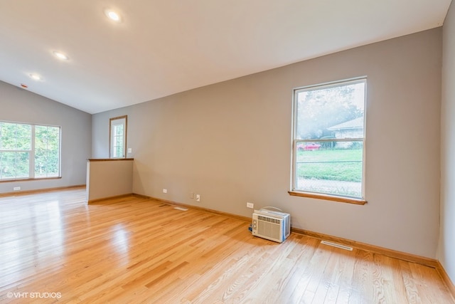 spare room with light wood-type flooring, lofted ceiling, and a wall mounted air conditioner