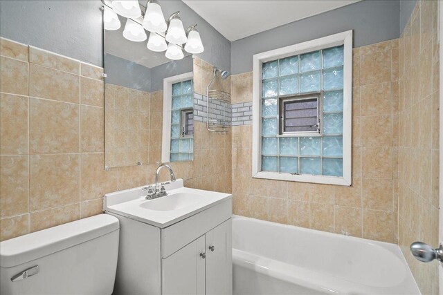 full bathroom with tile walls, vanity, toilet, and tiled shower / bath